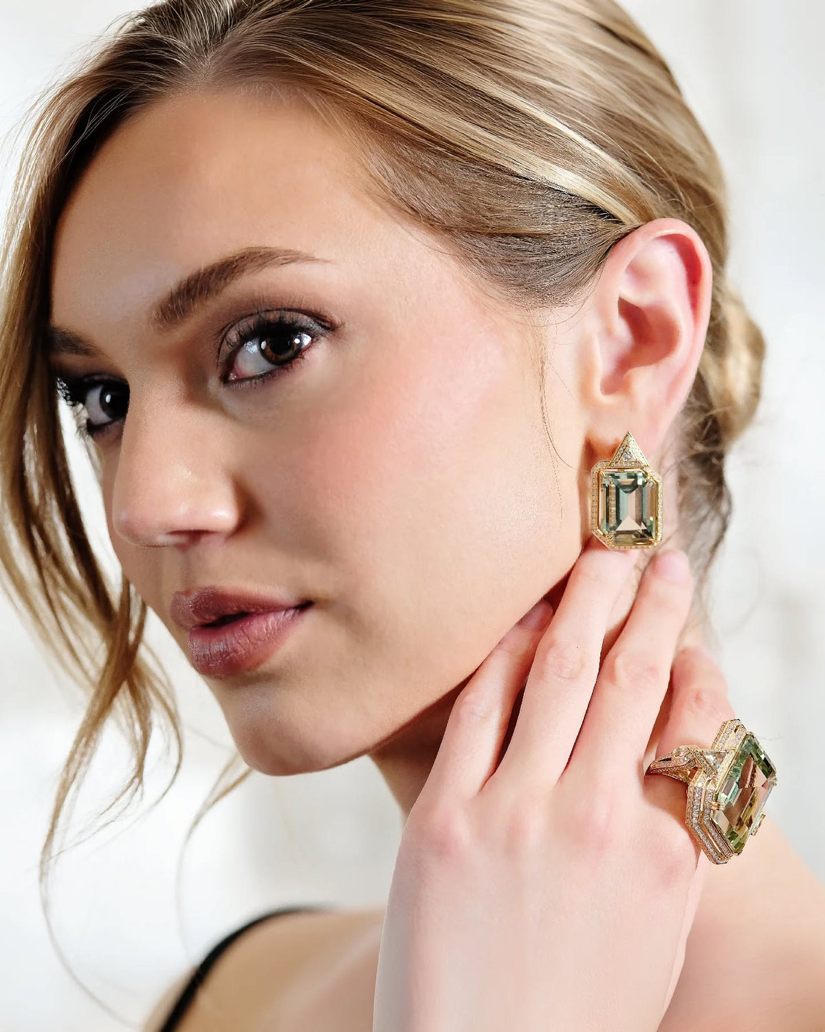 Woman wearing green gemstone drop earrings in yellow gold with a matching statement ring